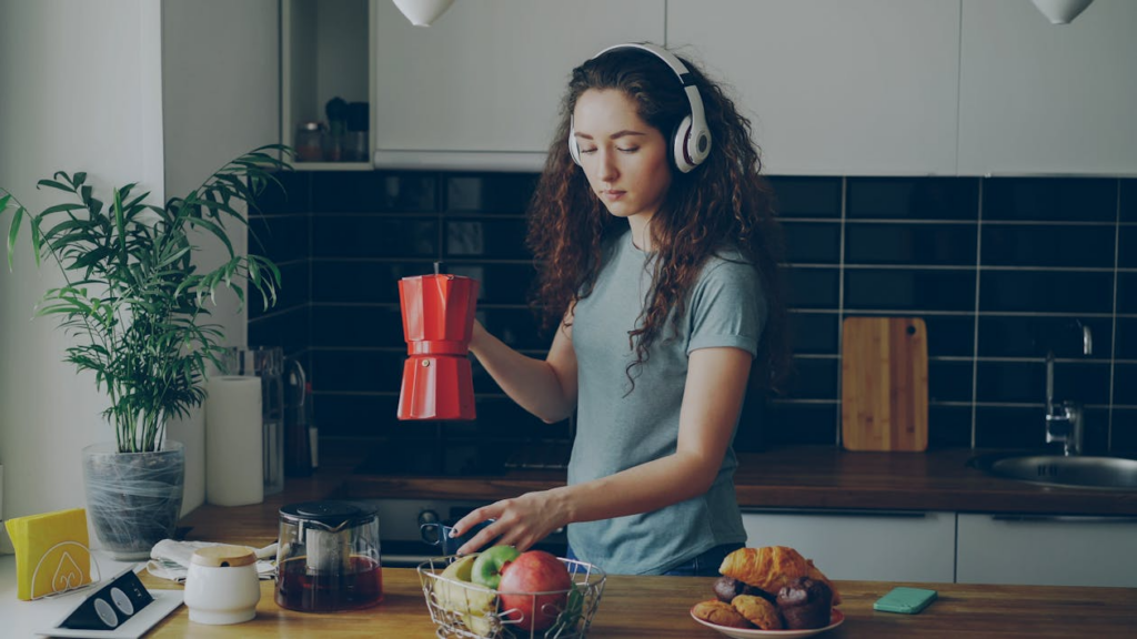 Woman wearing headphones as background news consumption while preparing breakfast.