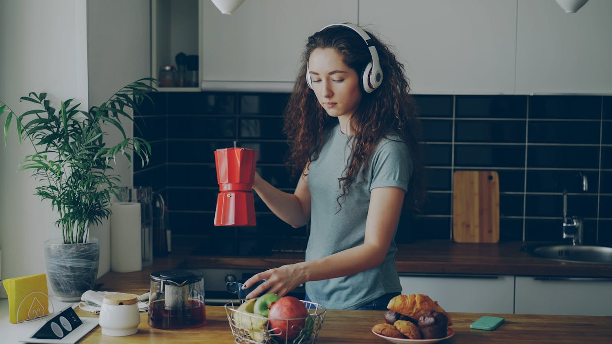 Woman wearing headphones as background news consumption while preparing breakfast.