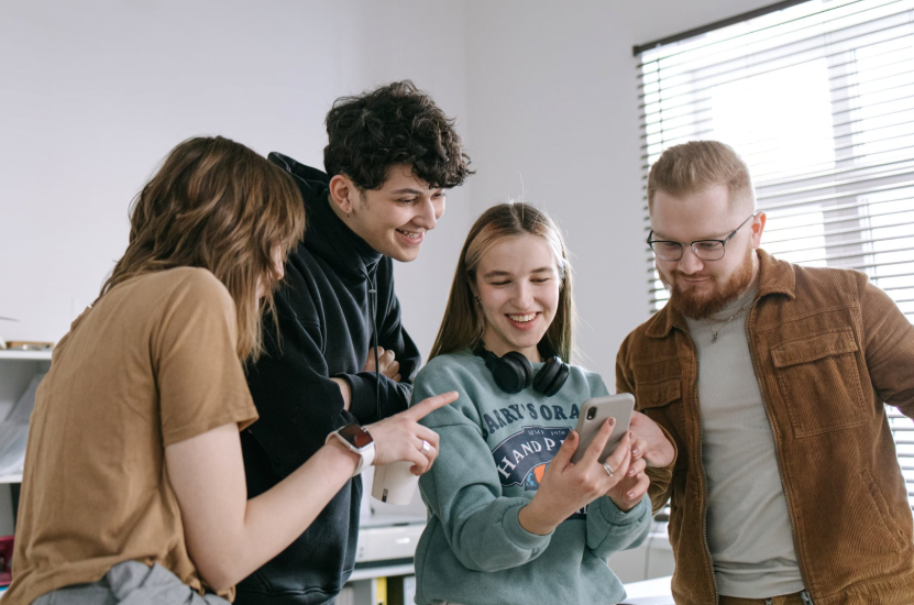 Friends laughing at a content in a phone showing how internet humor evolved.